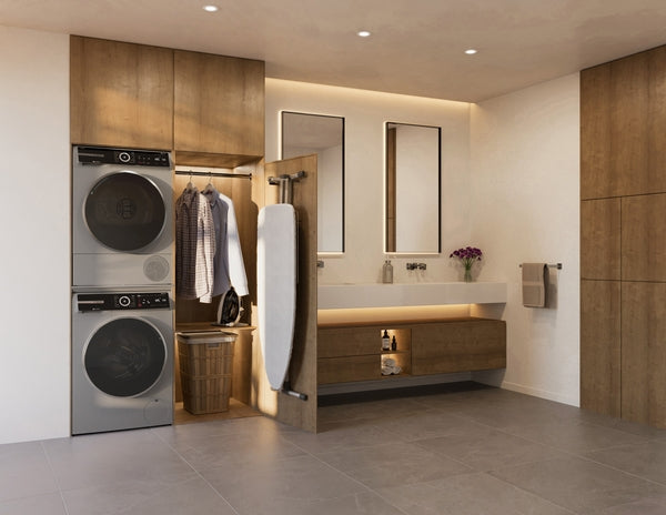 Stacked pearl steel Bosch front load washers integrated in stylish laundry room with wooden cabinets and ironing board nearby