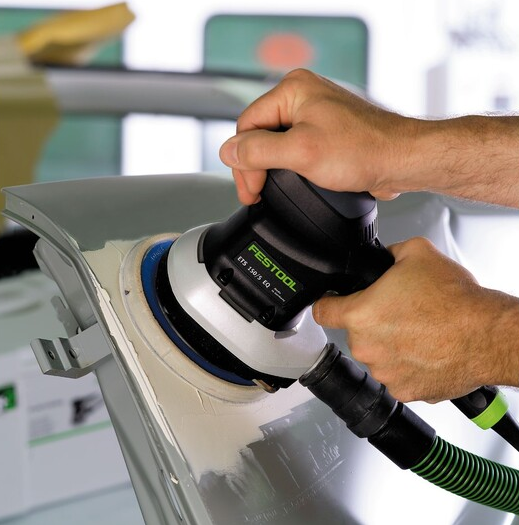 Person using a Festool power sander with dust extraction on car body panel in home improvement and woodworking tasks