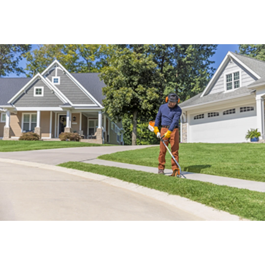 Person using orange and white battery-powered edger to trim grass along a sidewalk in a residential neighborhood