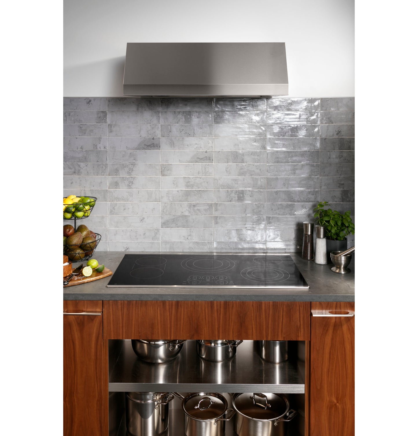 Modern built-in electric cooktop with smooth surface on wood cabinetry and gray tile backsplash in kitchen setting