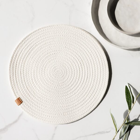 Ivory round woven placemat with concentric circle pattern on marble surface with ceramic bowls and green leaves