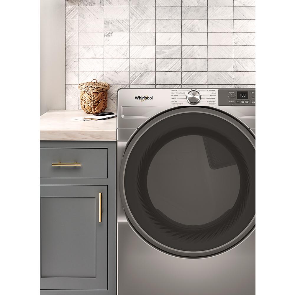 Front load smart electric dryer in stainless steel finish next to gray cabinetry with brass handles in laundry setting
