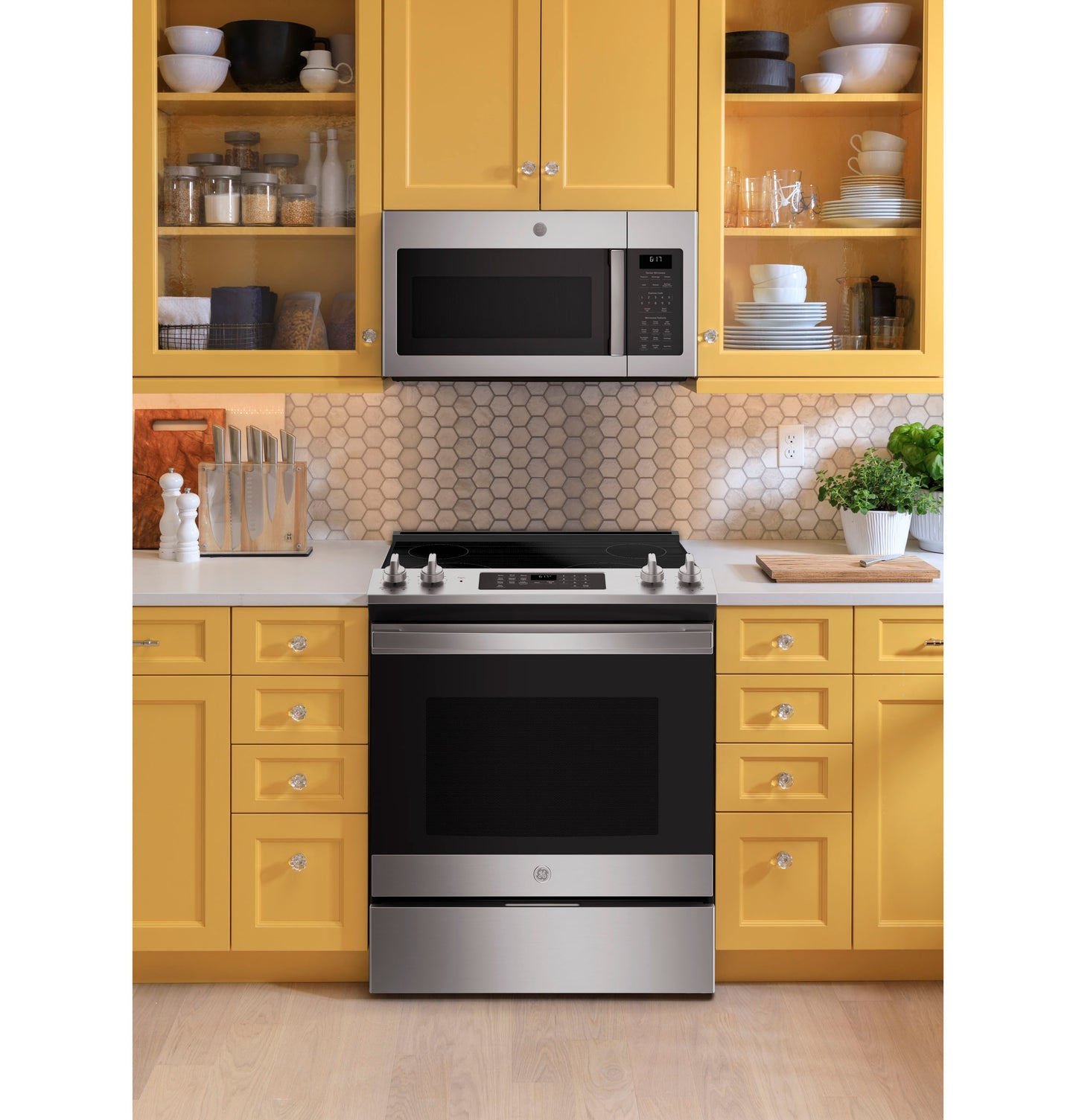 Over-the-range microwave in stainless steel above matching smooth top electric range in yellow kitchen setting with hex tile backsplash