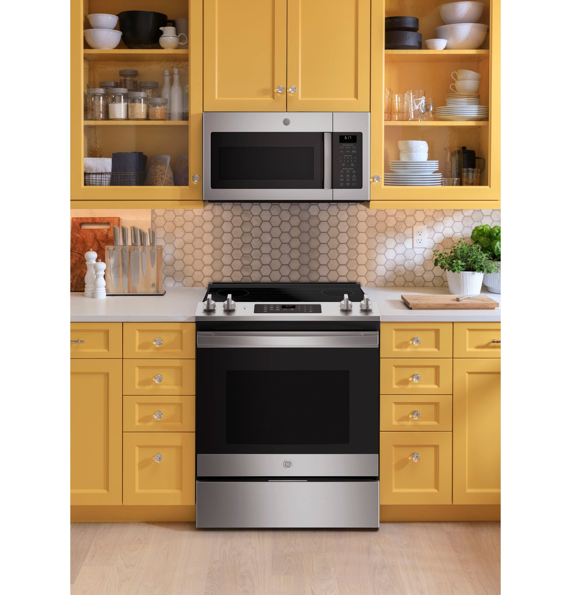 Over-the-range microwave in stainless steel above matching smooth top electric range in yellow kitchen setting with hex tile backsplash