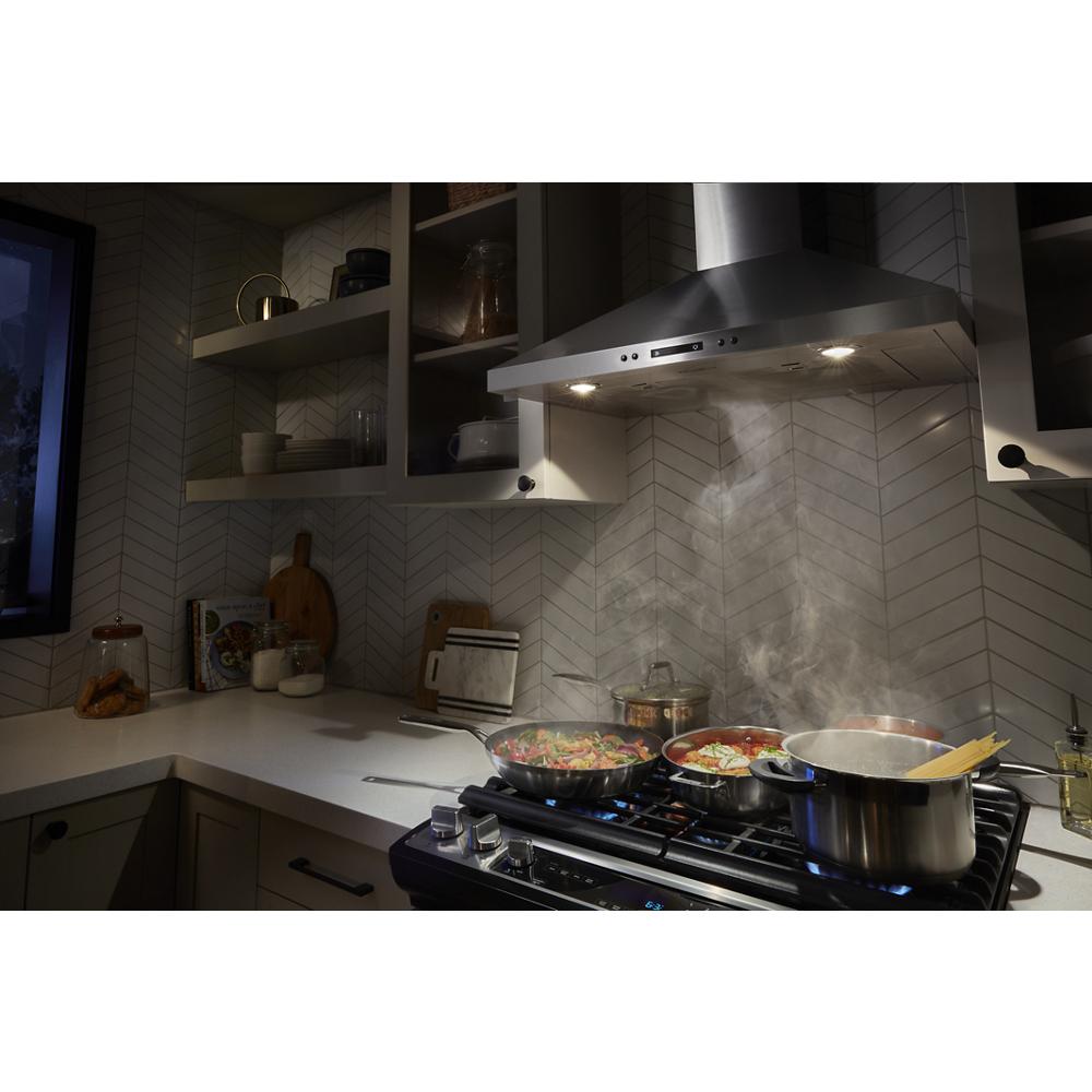 Stainless steel chimney range hood with LED lights, installed above a stove with pots and pans steaming in a modern kitchen