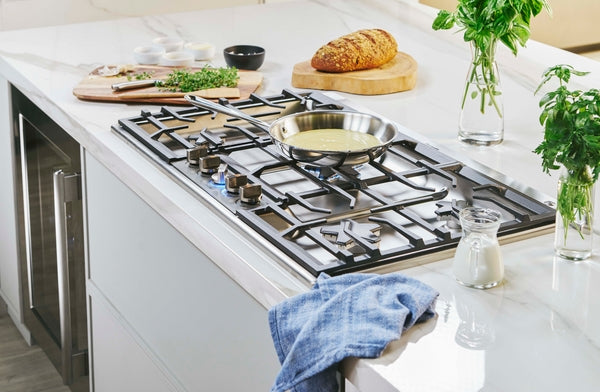 36-inch stainless steel gas cooktop with skillet cooking on Star® Burner and fresh bread on white kitchen countertop