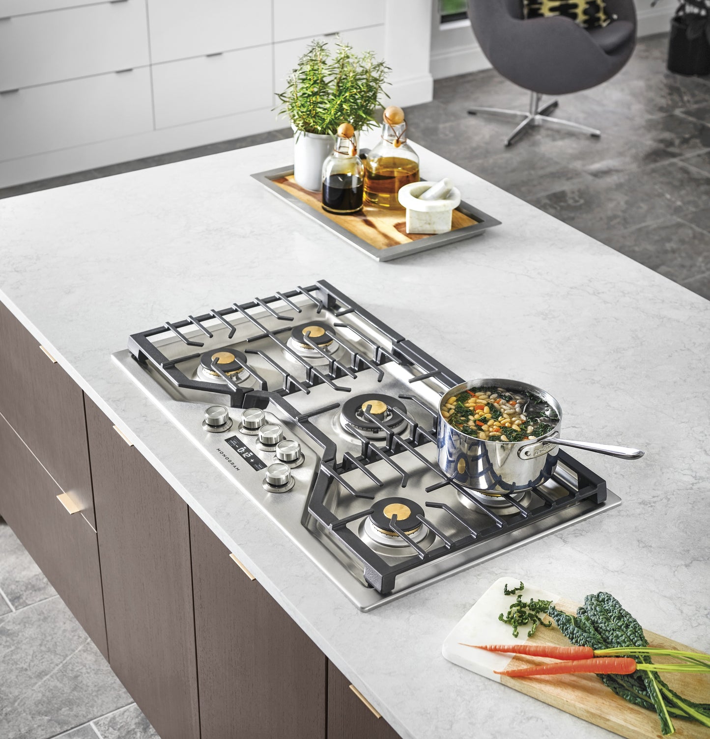 Modern stainless steel gas cooktop with brass burner caps and black cast iron grates in a kitchenware and appliance setting