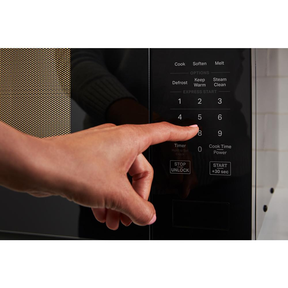Hand pressing number 8 on black microwave touch control panel with presets for cooking and steaming functions.