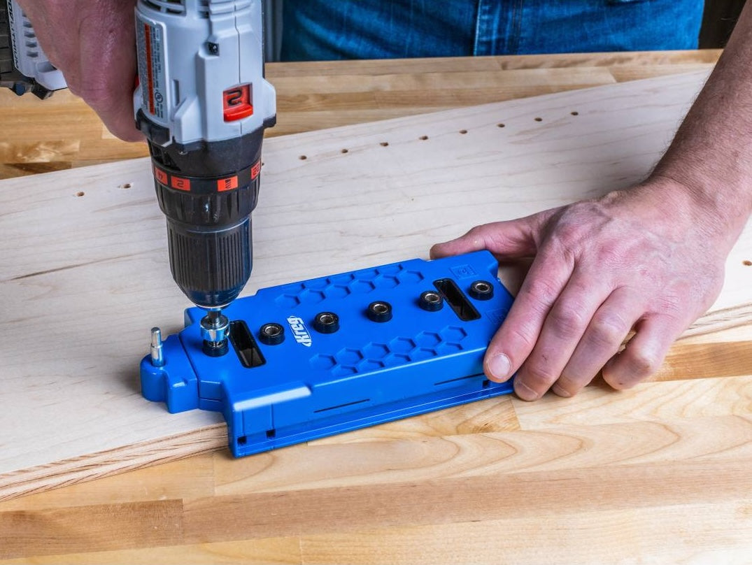 Blue woodworking jig with metal guide bushings used for drilling precise shelf pin holes in wood projects