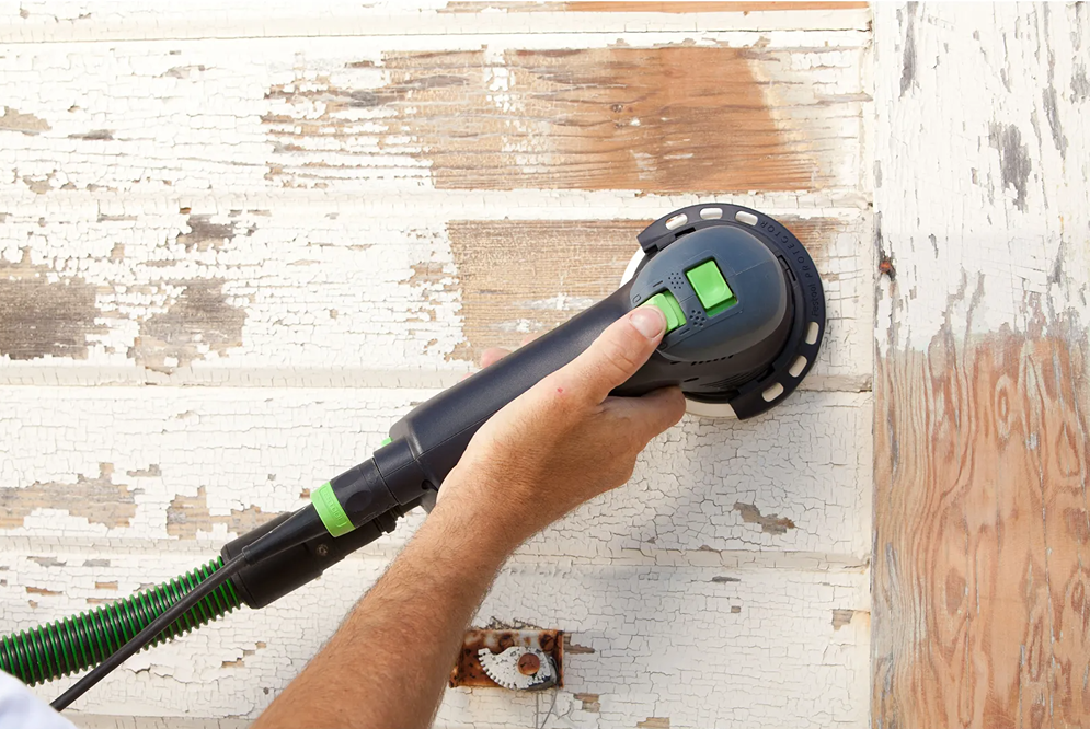 Hand operating a dual mode sander on peeling wood siding for surface restoration in home improvement projects