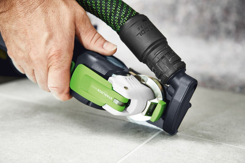 Hand gripping a green and black Festool dust extractor attachment removing grout from tile seams during home improvement tasks