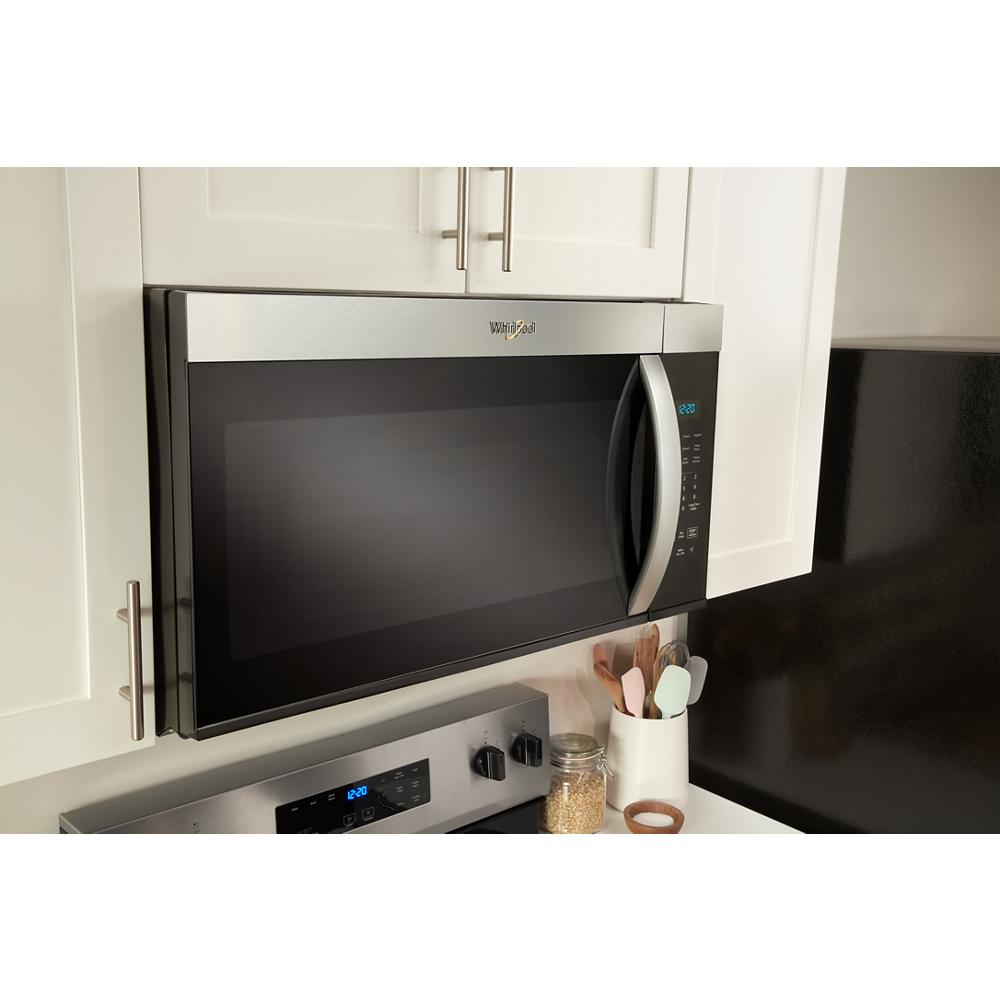 Stainless steel over-the-range microwave installed above stove with control panel and curved handle in kitchen setup