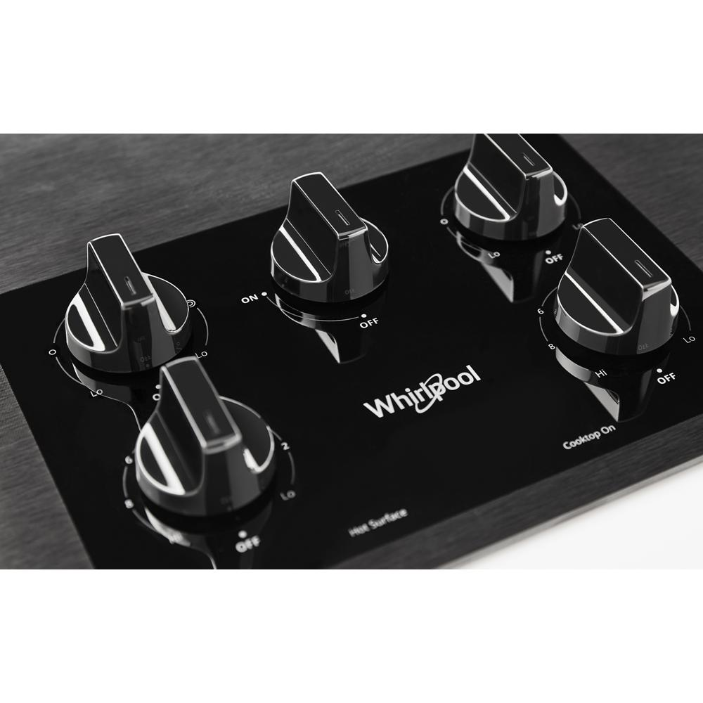Close-up of black ceramic cooktop control panel with five knobs and Whirlpool logo in kitchen appliance setting