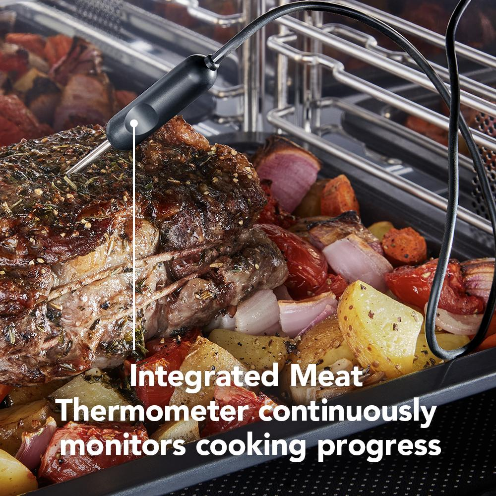 Close-up of seasoned roast with meat thermometer probe cooking alongside roasted vegetables in oven rack tray