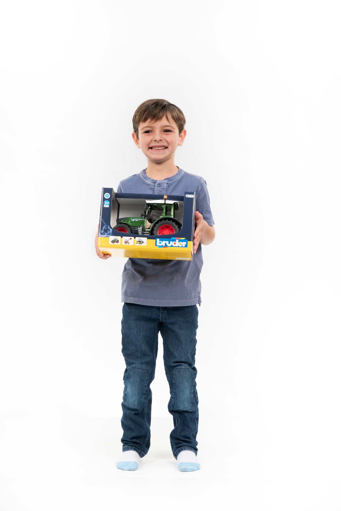 Smiling child holding a boxed Bruder Fendt Vario 211 tractor toy, suitable for tools and home improvement fans