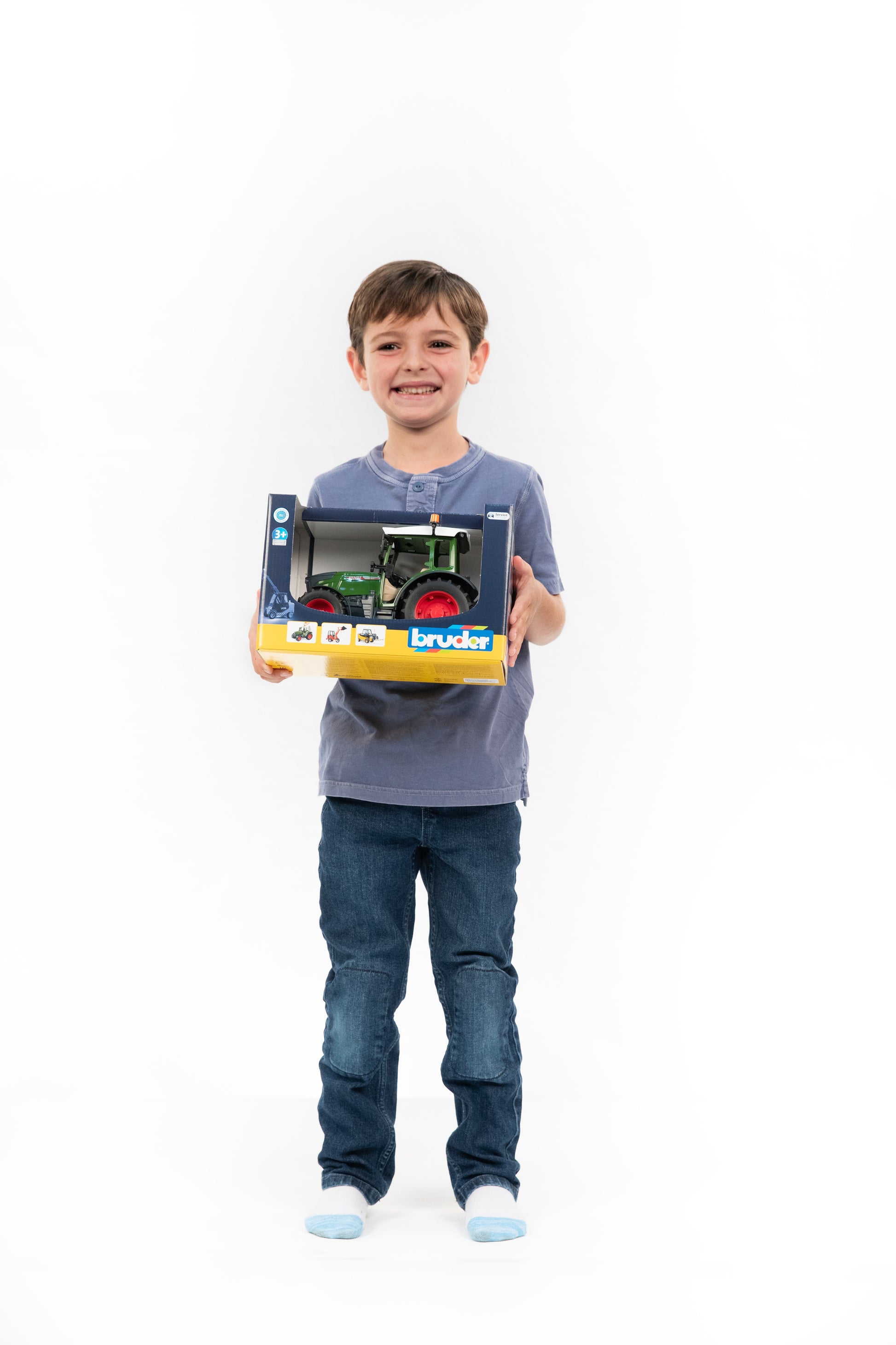 Smiling child holding a boxed Bruder Fendt Vario 211 tractor toy, suitable for tools and home improvement fans