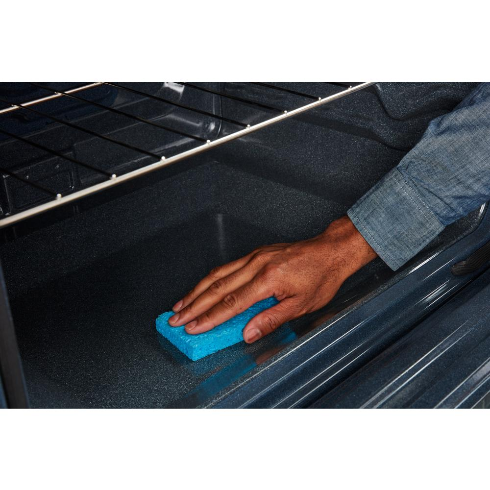 Hand wiping the interior bottom of a spacious oven cavity with a blue cleaning sponge in a kitchen appliance.