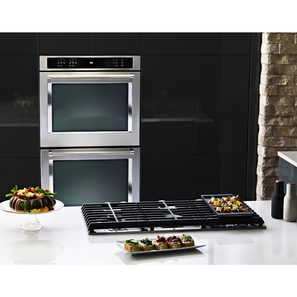 Modern kitchen scene with double stainless steel wall ovens, black gas cooktop, and plated appetizers on white countertop