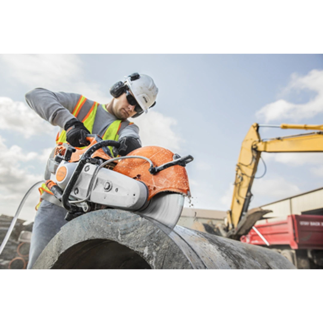 Worker wearing safety gear using a STIHL power cutter with water spray to cut a large concrete pipe outdoors