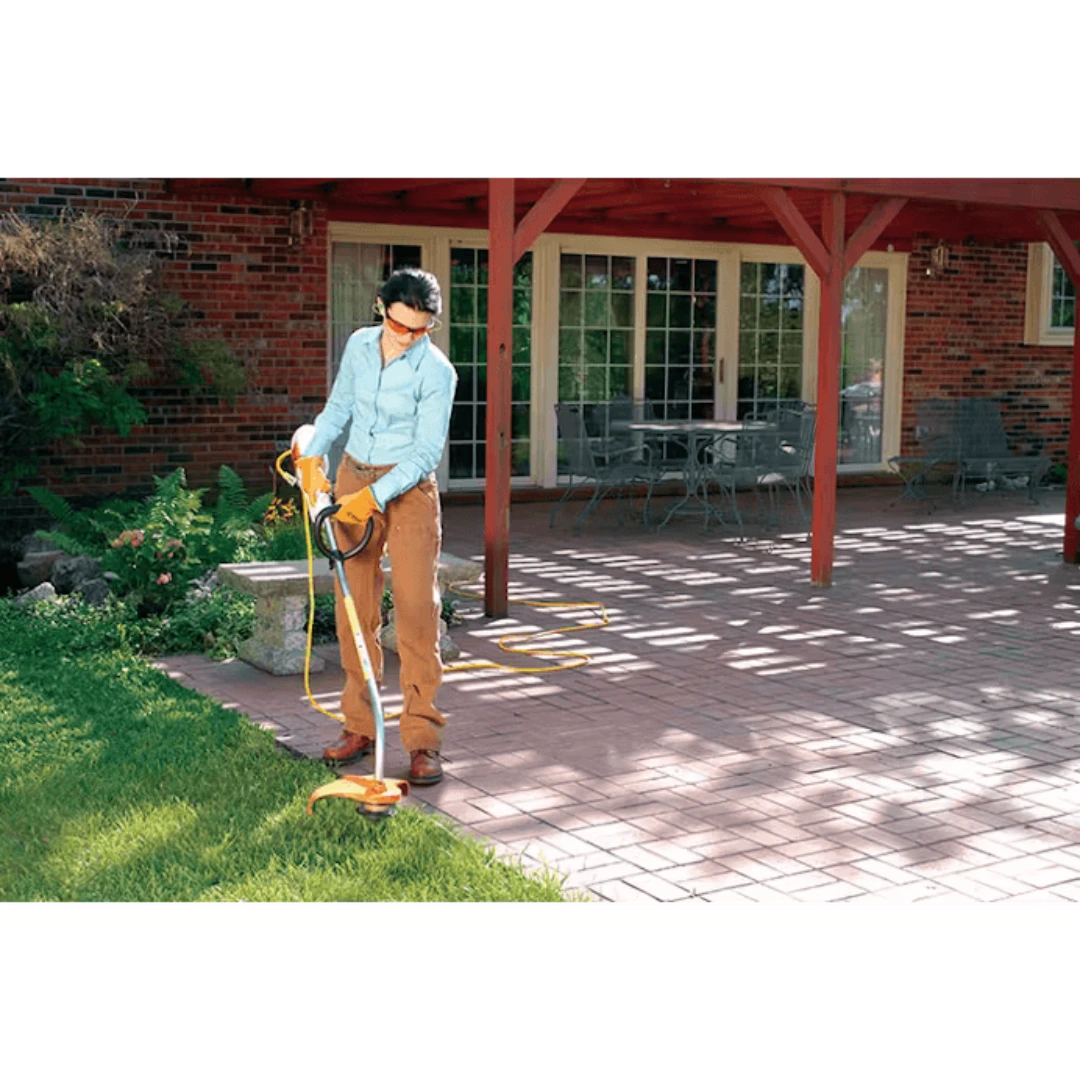 Person trimming grass edge with orange-handled electric garden tool near patio and brick house background