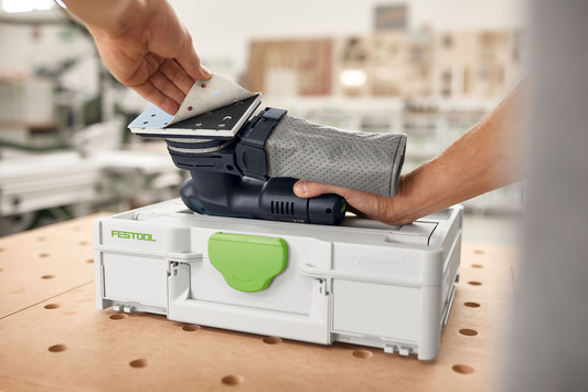 Hand attaching gray abrasive sanding sheet to black Festool sander on white Systainer for tool accessories and home improvement