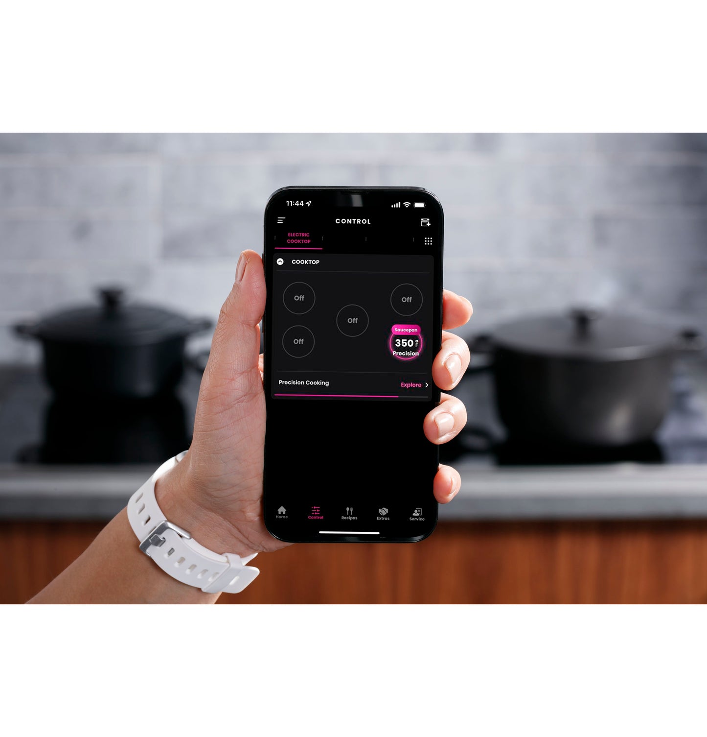 Hand holding smartphone showing remote control app for induction cooktop in modern kitchen setting