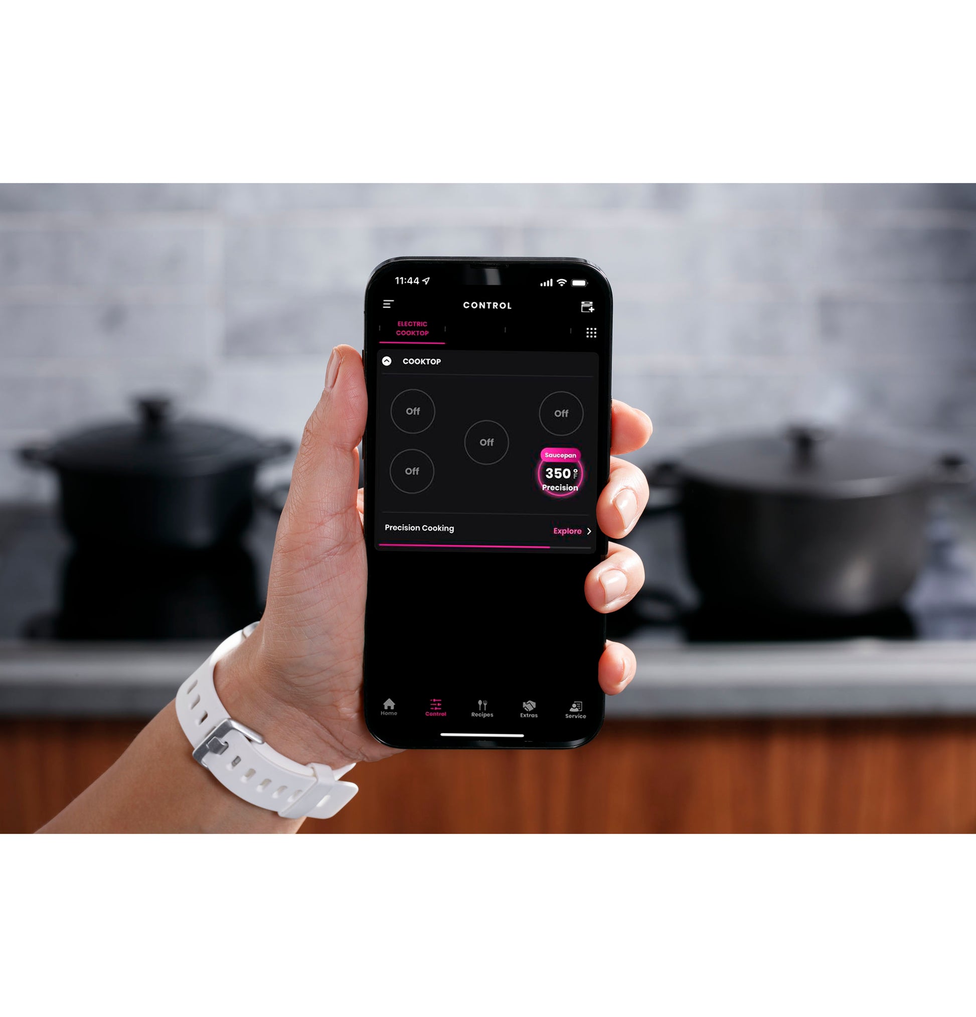 Hand holding smartphone showing remote control app for induction cooktop in modern kitchen setting