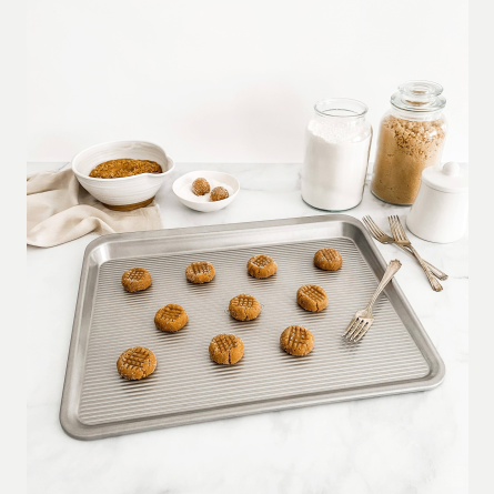 Textured metal cookie tray pan with freshly baked cookies and baking ingredients for kitchenware and bakeware uses under $50 collections