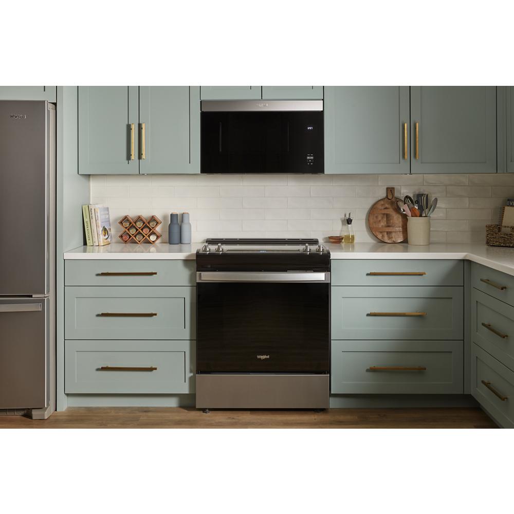 Built-in microwave with black glass front above stainless steel range in kitchen with green cabinetry and brass handles
