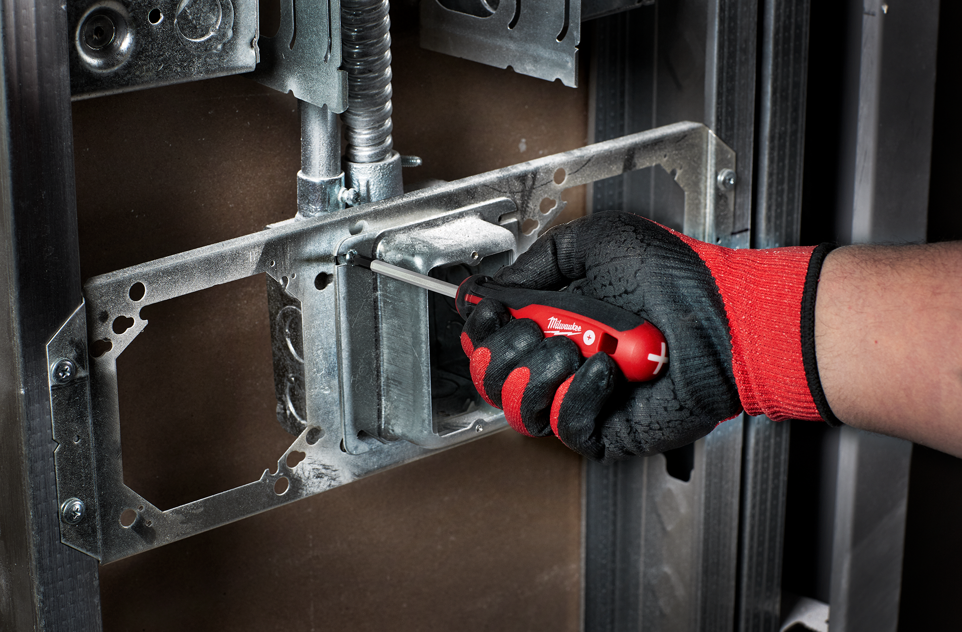 Hand wearing red and black glove using red screwdriver with ergonomic handle to install electrical box frame in home improvement setting