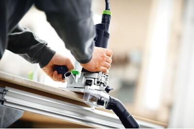 Person guiding Festool trim router along metal rail for accurate cutting in woodwork and home improvement tasks