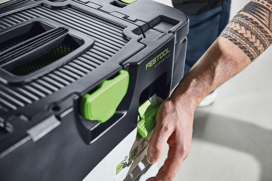 Hand gripping green latch on black and green compact Festool cordless dust extractor for tools and home improvement tasks