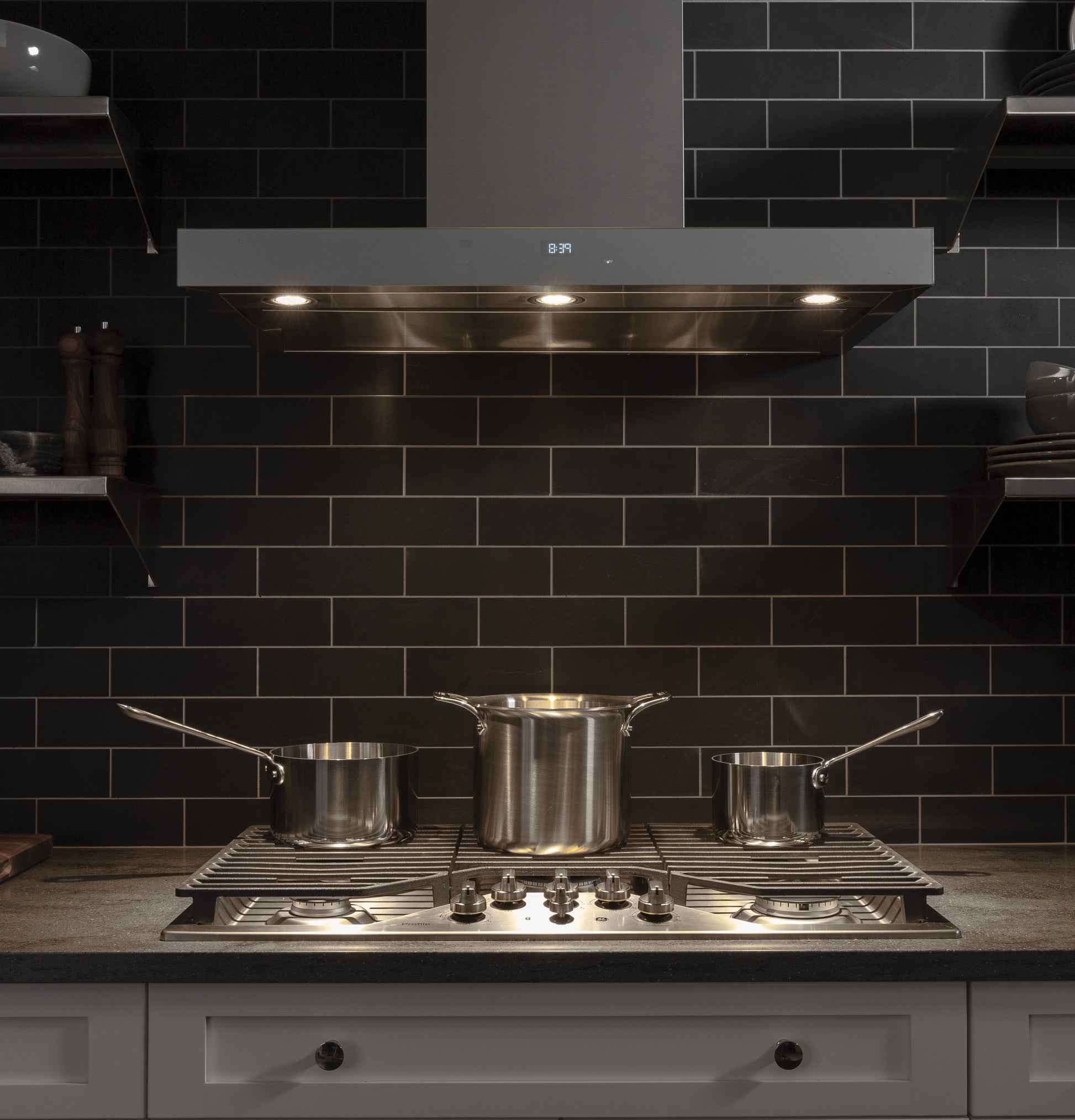 Modern stainless steel gas cooktop with five burners and grates under a vent hood in a kitchen setting