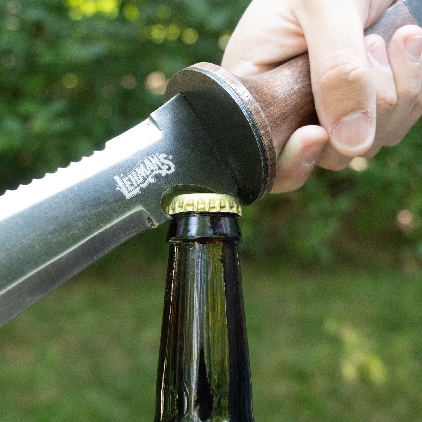 Close-up of wooden-handled hori hori knife with serrated blade opening bottle cap in outdoor garden setting