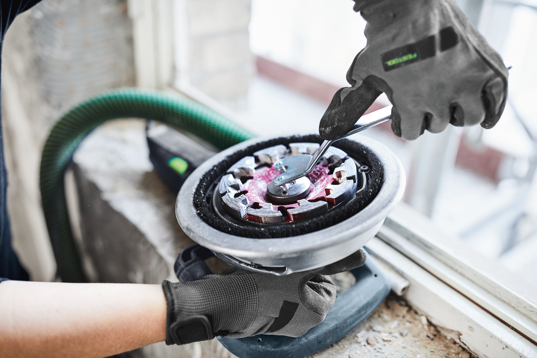 Person tightening adjustment screw on Festool diamond grinder with dust extraction hose in home improvement setting
