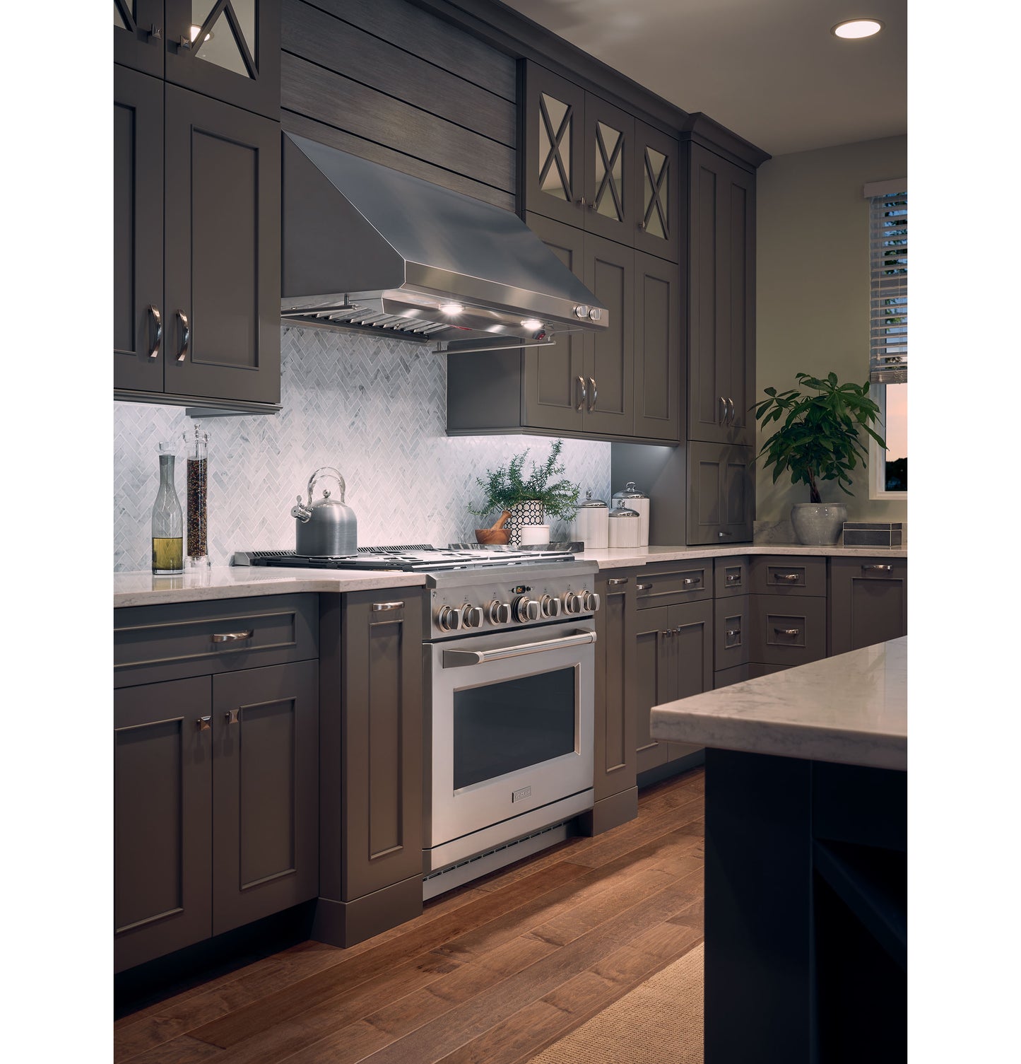 Kitchen featuring Monogram stainless steel professional hood over range with dark cabinetry and wood flooring