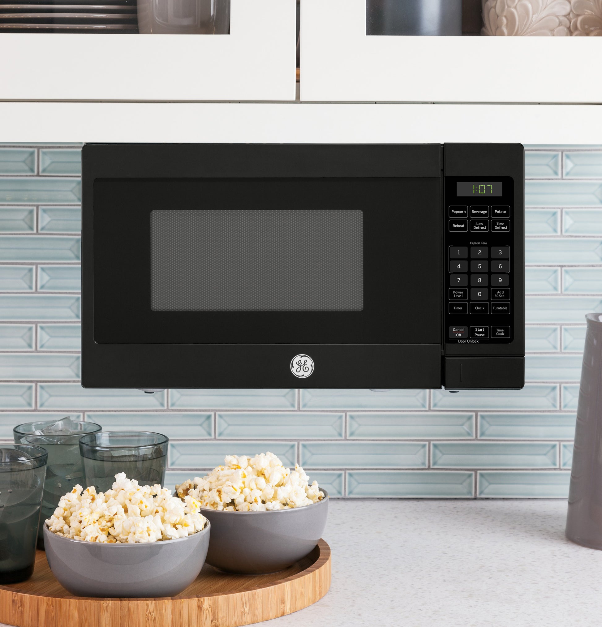 Black compact countertop microwave with digital keypad, LED timer display, and glass bowl of popcorn in kitchen setting