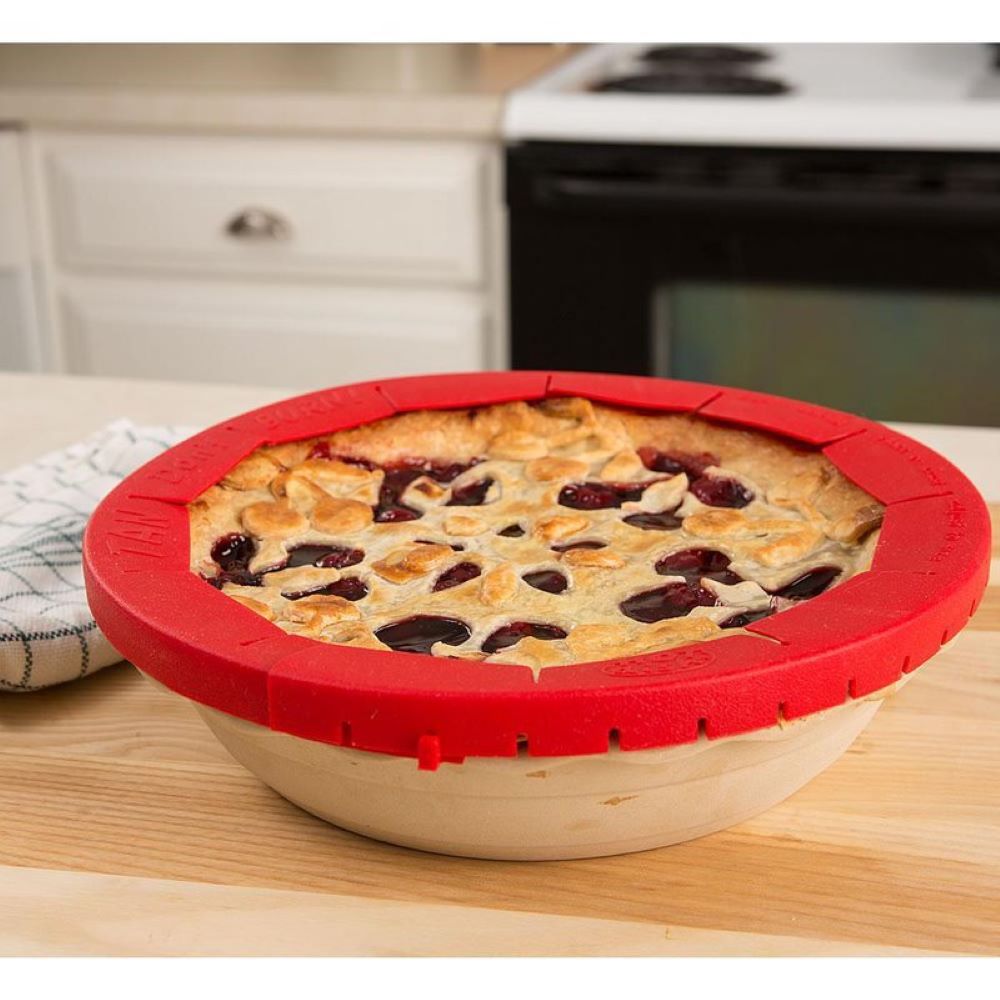 Red silicone adjustable pie crust shield protecting edges of a baked fruit pie for kitchenware use