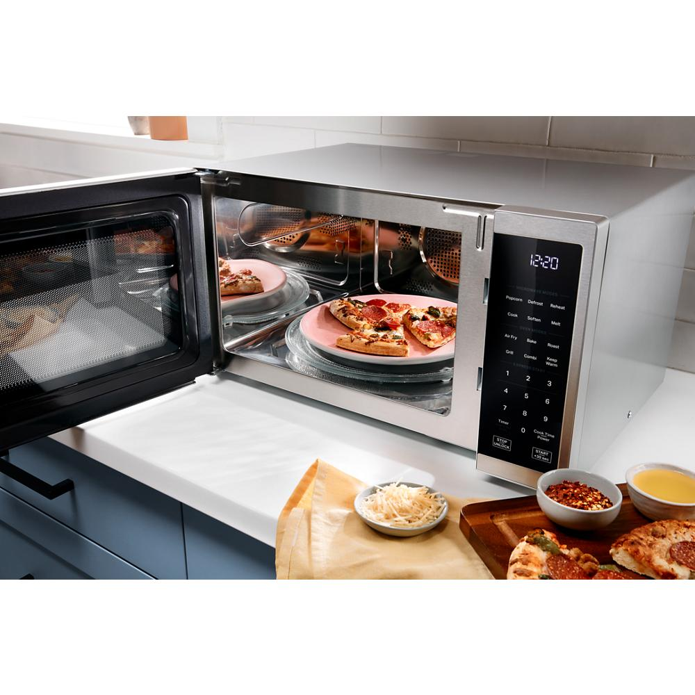 Stainless steel countertop microwave with air fry and grill modes cooking pizza on a glass turntable in kitchen setting