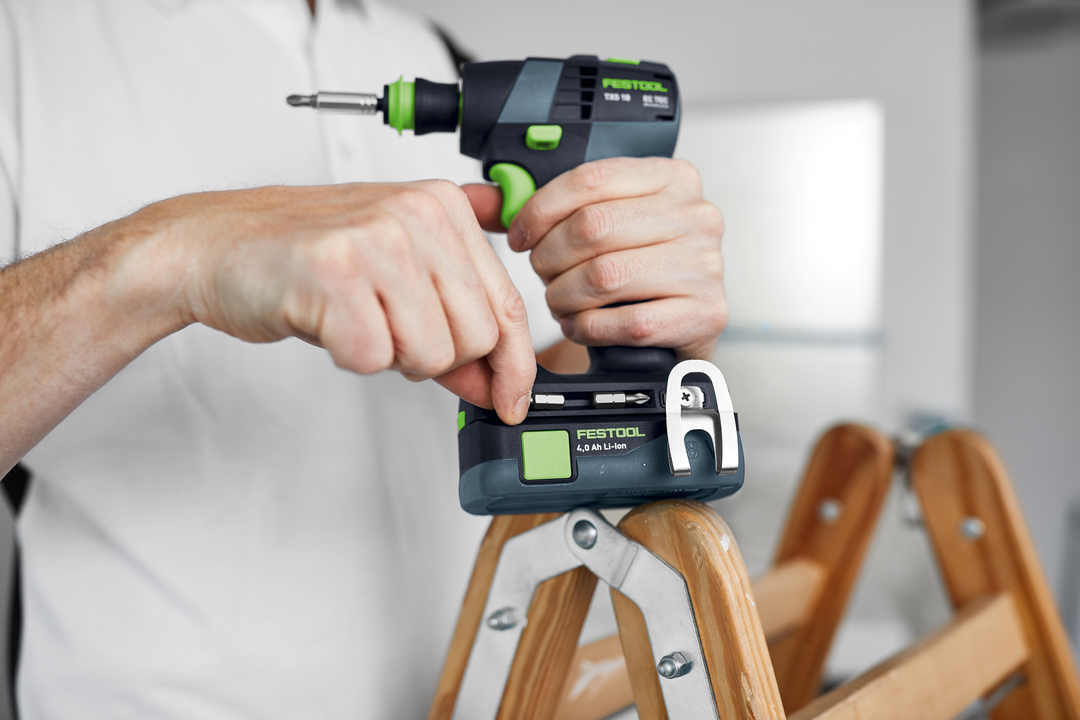 Person adjusting a compact Festool cordless drill resting on a wooden ladder for home improvement tasks