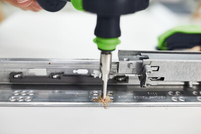 Close-up of a drill with a Centrotec bit installing metal drawer slides in a home improvement setting