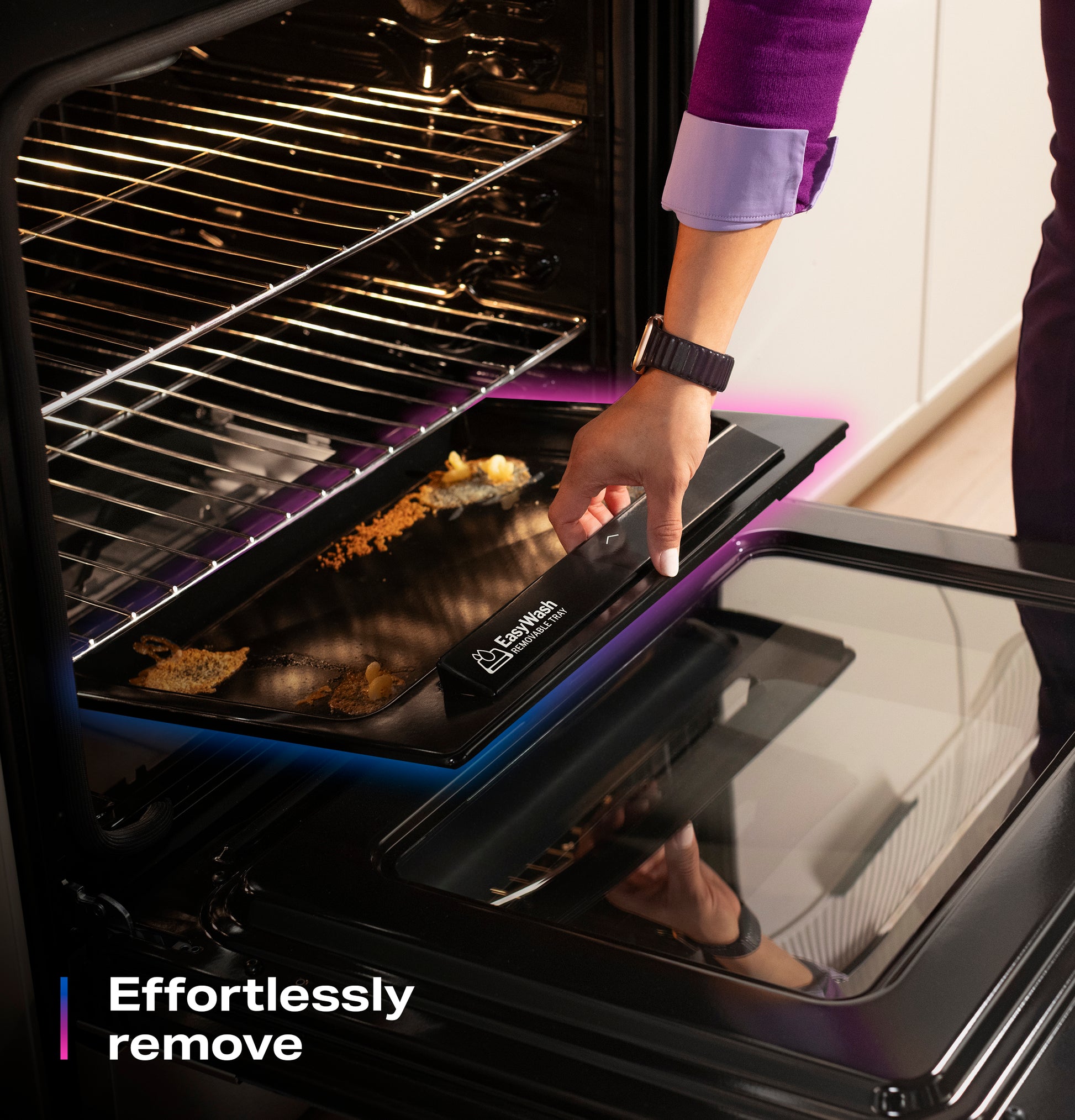 Hand lifting EasyWash™ oven tray with baked food residue from open electric convection oven in kitchen setting