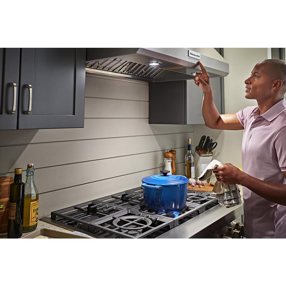 Man adjusting stainless steel wall-mount canopy range hood over gas stove with blue pot in modern kitchen appliances setting