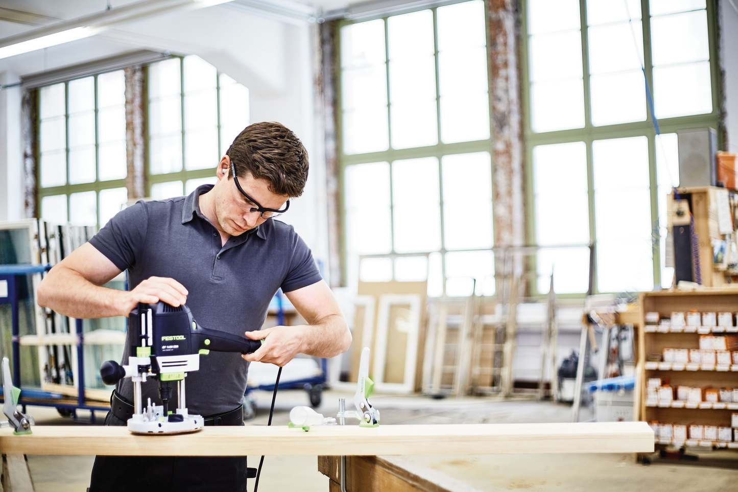 Man using a Festool router on wood in a bright woodworking shop for home improvement and power tool accessories