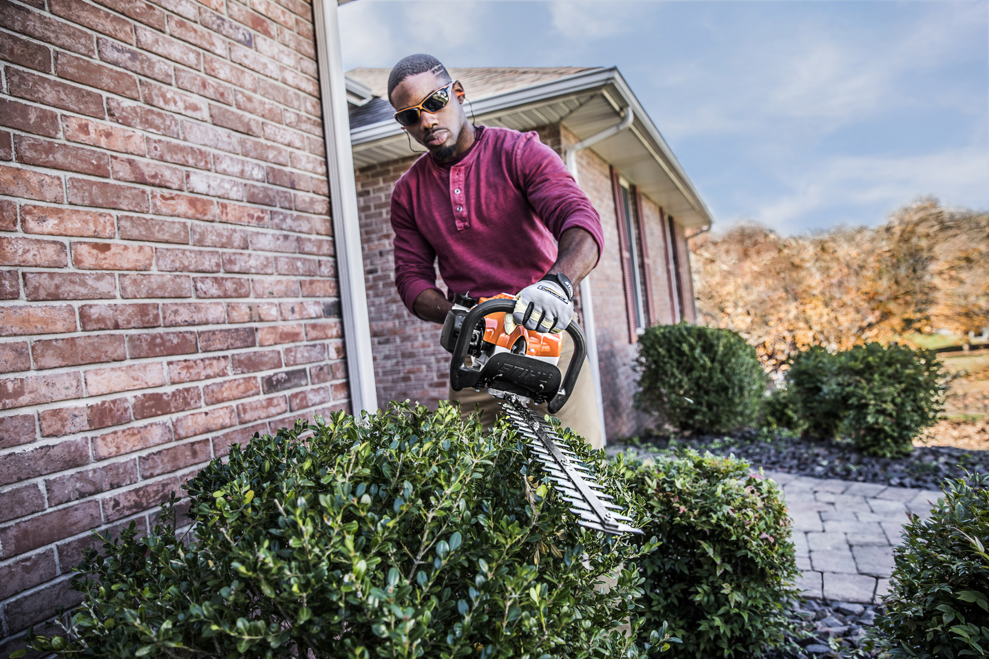 Man using orange and black STIHL lightweight hedge trimmer to shape outdoor shrubbery in a home improvement setting