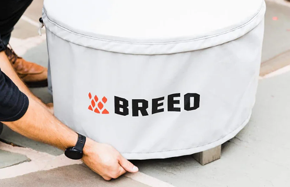 Light gray fire pit cover with Breeo logo, fitted onto round fire pit for outdoor protection