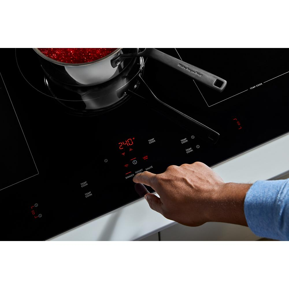 Hand adjusting digital controls on black induction cooktop with five cooking zones in modern kitchen setting