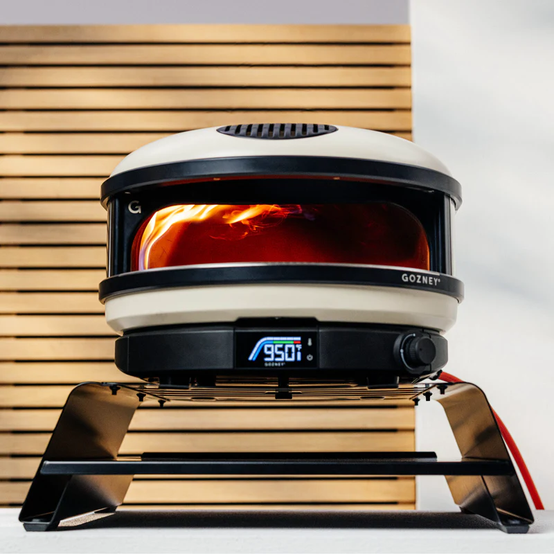 Compact pizza oven with digital temperature display, set on a sturdy metal booster stand in outdoor grilling accessories collection