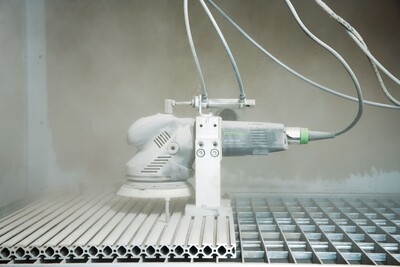Automated white multi-mode sander smoothing metal grates with attached power cables for tools and home improvement use