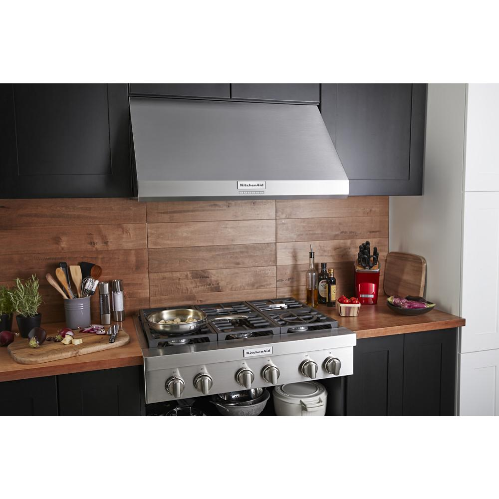 Stainless steel commercial-style wall-mount canopy range hood above gas stove in modern kitchen setting